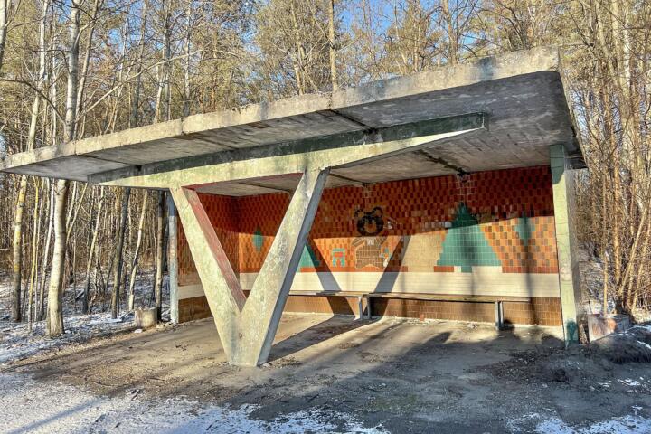 A weathered concrete Soviet bus shelter with a mosaic mural on its back wall, photographed in snow near Chernobyl