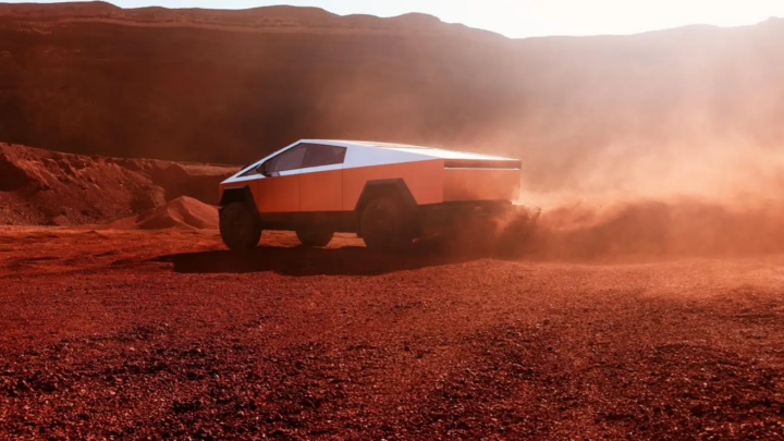 A Tesla Cybertruck driving across reddish desert terrain, kicking up dust behind its rear wheels under a hazy orange sky